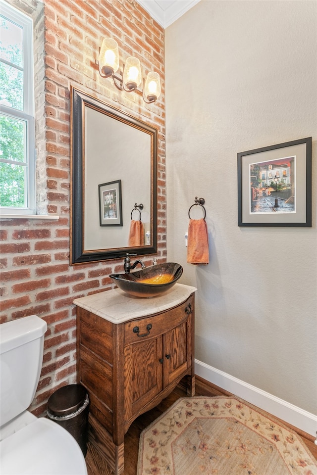 bathroom featuring brick wall, crown molding, hardwood / wood-style floors, toilet, and vanity