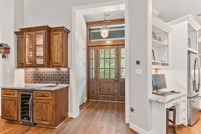 kitchen featuring beverage cooler, light hardwood / wood-style flooring, tasteful backsplash, light stone counters, and stainless steel refrigerator