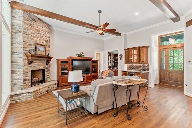 living room featuring beam ceiling, ceiling fan, crown molding, light hardwood / wood-style floors, and a fireplace