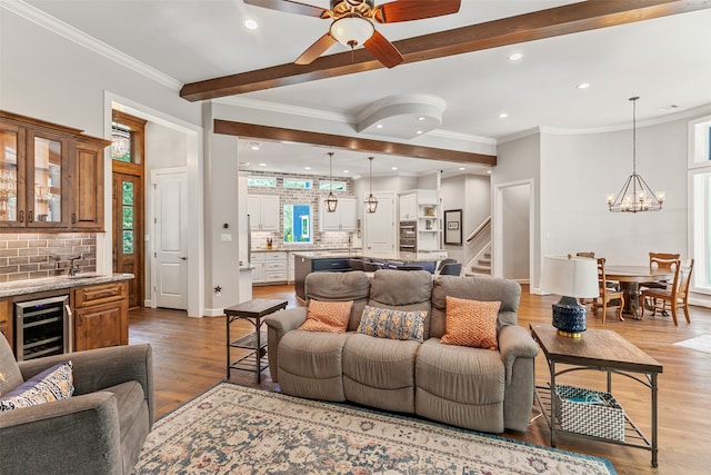 living room with ceiling fan with notable chandelier, plenty of natural light, beverage cooler, and crown molding