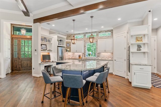 kitchen with white cabinetry, light stone counters, pendant lighting, a kitchen island with sink, and a breakfast bar