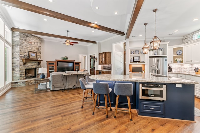 kitchen with a large island with sink, a fireplace, tasteful backsplash, white cabinetry, and stainless steel appliances