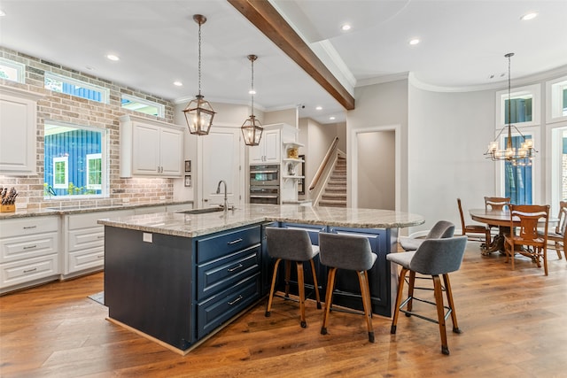 kitchen featuring white cabinets, a large island, sink, and decorative light fixtures