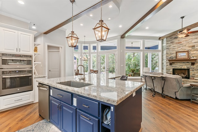 kitchen with a kitchen island with sink, white cabinets, a fireplace, blue cabinetry, and beam ceiling