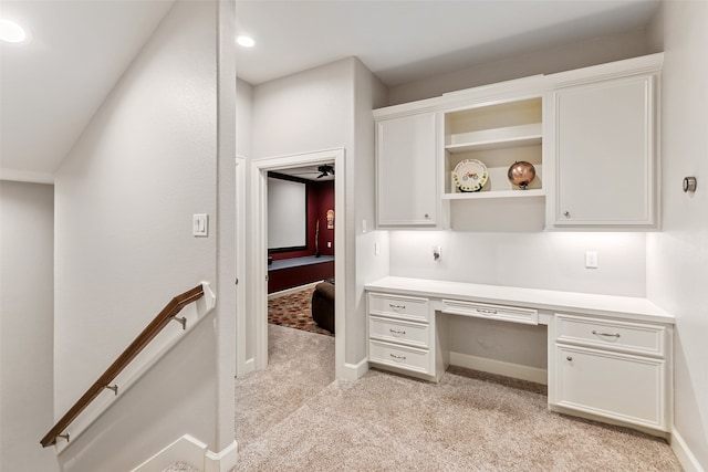 carpeted office space with built in desk and ceiling fan