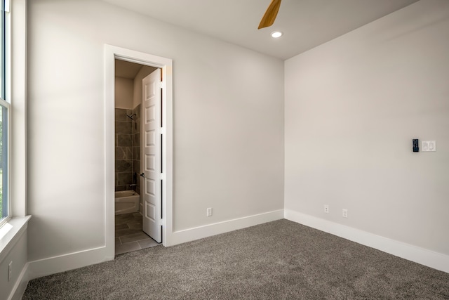 unfurnished bedroom featuring dark colored carpet, ceiling fan, and ensuite bath