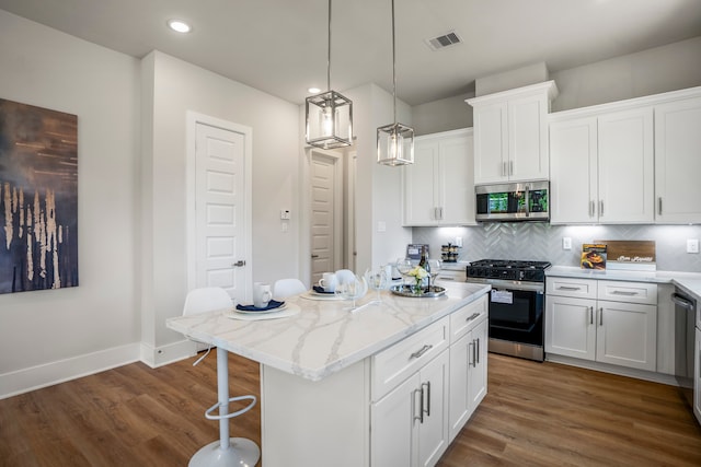 kitchen with pendant lighting, appliances with stainless steel finishes, a kitchen island, dark hardwood / wood-style flooring, and white cabinetry