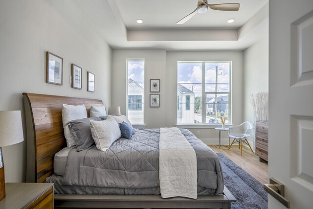 bedroom with hardwood / wood-style flooring, ceiling fan, and a raised ceiling