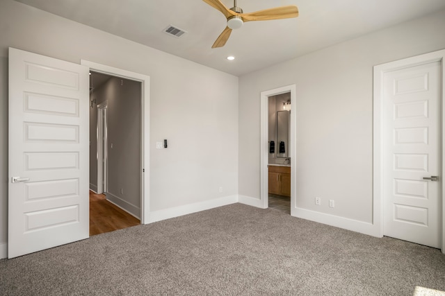 unfurnished bedroom featuring dark colored carpet, ensuite bath, and ceiling fan