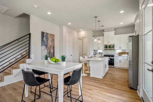 kitchen featuring white cabinetry, a center island, pendant lighting, appliances with stainless steel finishes, and light wood-type flooring