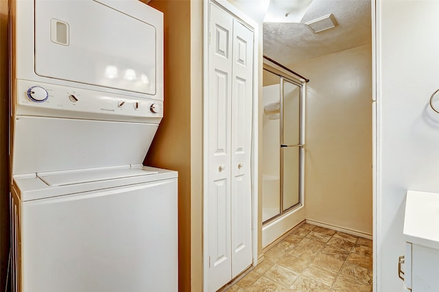 laundry area with stacked washer / drying machine, light tile patterned flooring, and a textured ceiling