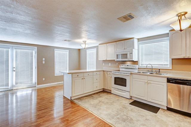 kitchen featuring visible vents, a sink, light countertops, white appliances, and a peninsula