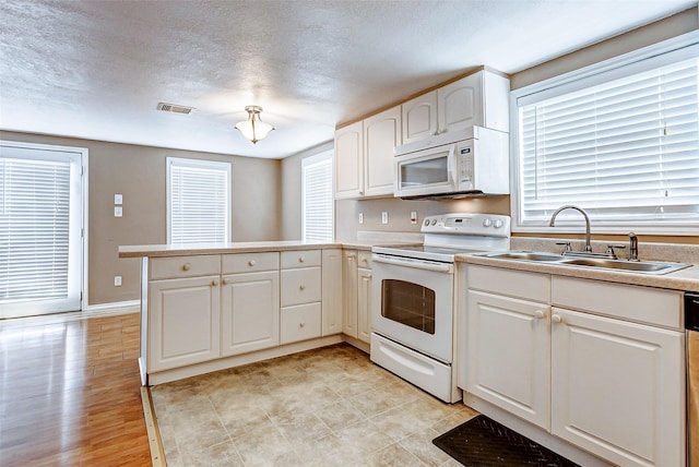 kitchen with white appliances, a peninsula, white cabinetry, visible vents, and a sink