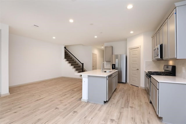 kitchen featuring light hardwood / wood-style flooring, gray cabinets, tasteful backsplash, an island with sink, and appliances with stainless steel finishes