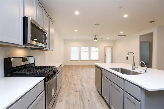 kitchen featuring ceiling fan, a kitchen island with sink, appliances with stainless steel finishes, light hardwood / wood-style floors, and sink