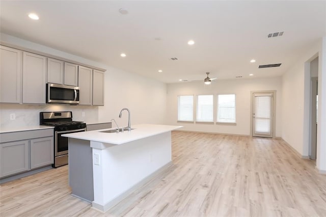 kitchen with light wood-type flooring, gray cabinetry, sink, a center island with sink, and stainless steel appliances