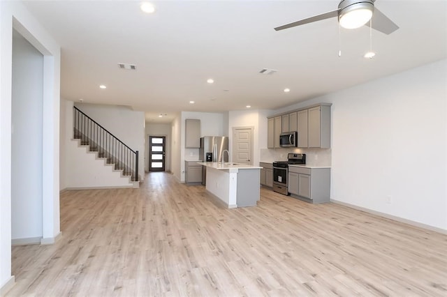 kitchen featuring ceiling fan, gray cabinets, appliances with stainless steel finishes, light hardwood / wood-style floors, and a center island with sink