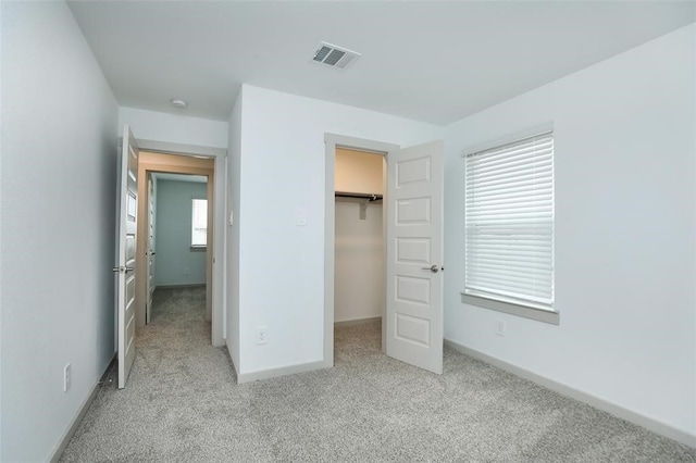 unfurnished bedroom featuring multiple windows, light carpet, a spacious closet, and a closet