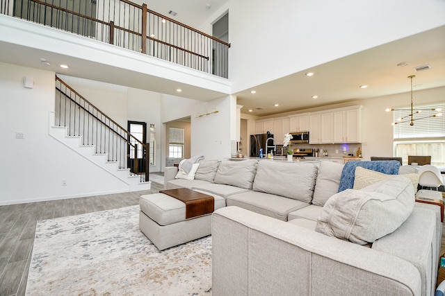 living room with light hardwood / wood-style floors, a towering ceiling, plenty of natural light, and a chandelier