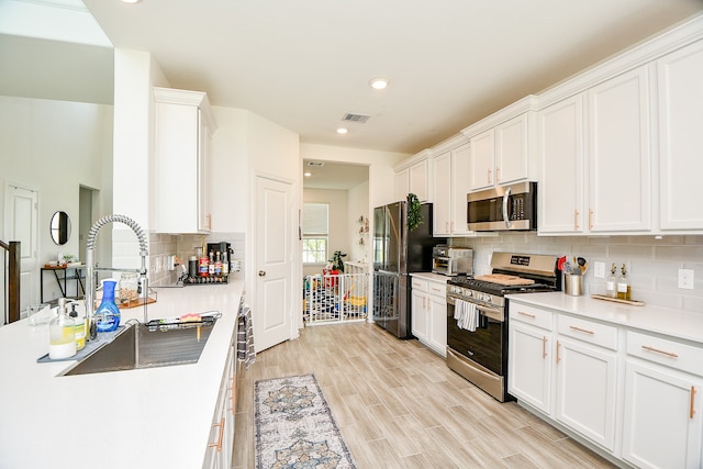 kitchen featuring backsplash, sink, light hardwood / wood-style floors, white cabinetry, and stainless steel appliances