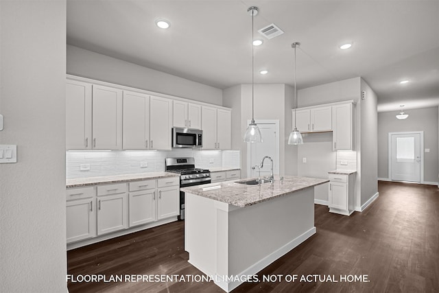 kitchen featuring light stone countertops, appliances with stainless steel finishes, decorative light fixtures, white cabinetry, and an island with sink