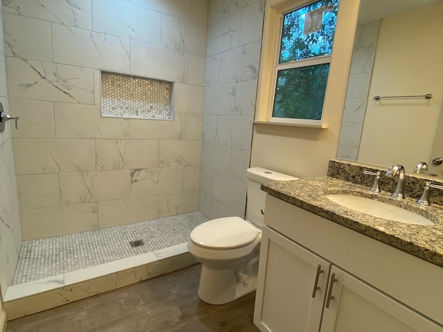 bathroom with toilet, hardwood / wood-style floors, vanity, and a tile shower