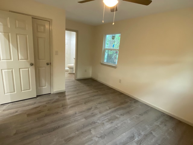 unfurnished bedroom featuring hardwood / wood-style flooring, a closet, connected bathroom, and ceiling fan