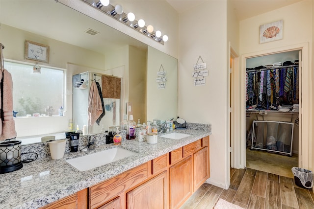 full bathroom with wood finish floors, a sink, visible vents, a spacious closet, and double vanity