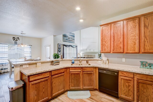 kitchen with black dishwasher, light wood-style flooring, a sink, light stone countertops, and a peninsula