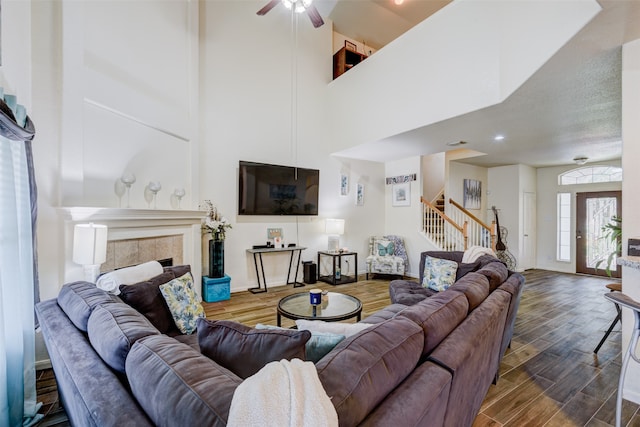 living room featuring dark wood-type flooring, a high ceiling, a tiled fireplace, and ceiling fan