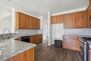 kitchen featuring sink, kitchen peninsula, light stone counters, dark hardwood / wood-style floors, and stainless steel gas range oven