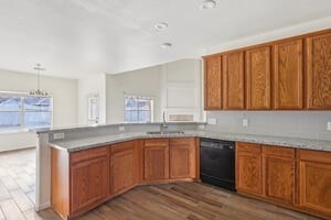 kitchen featuring black dishwasher, brown cabinets, wood finished floors, a peninsula, and a sink