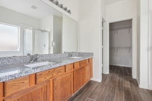 full bathroom featuring a sink, double vanity, a stall shower, and wood finished floors