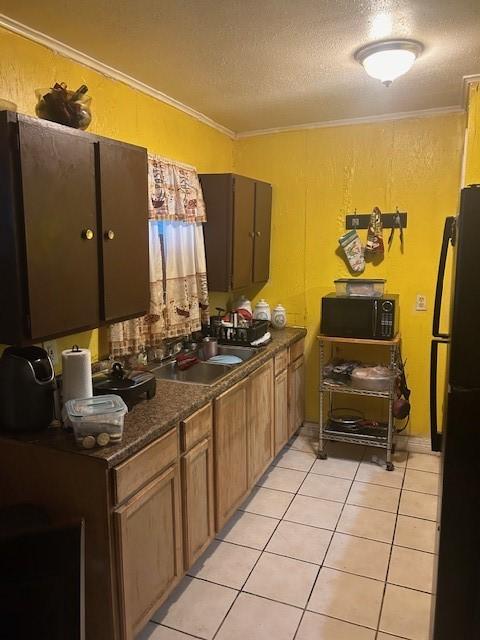 kitchen with light tile patterned floors, a textured ceiling, black appliances, dark countertops, and crown molding