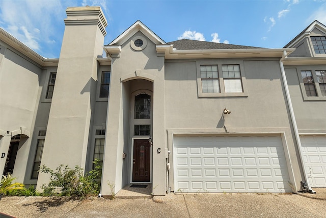 multi unit property with a garage, driveway, a chimney, and stucco siding