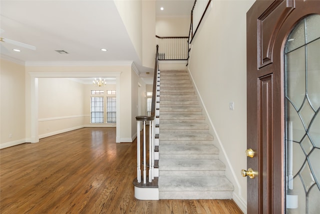 staircase with hardwood / wood-style flooring, crown molding, and a notable chandelier