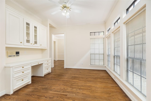 unfurnished office with dark wood-type flooring, ornamental molding, a healthy amount of sunlight, and built in desk