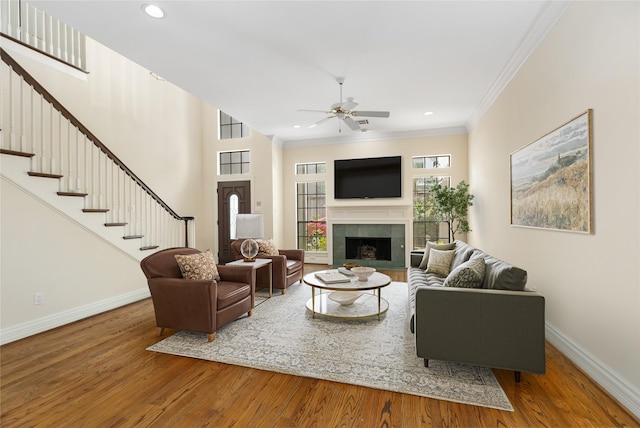 living room featuring ceiling fan, crown molding, a fireplace, and wood-type flooring