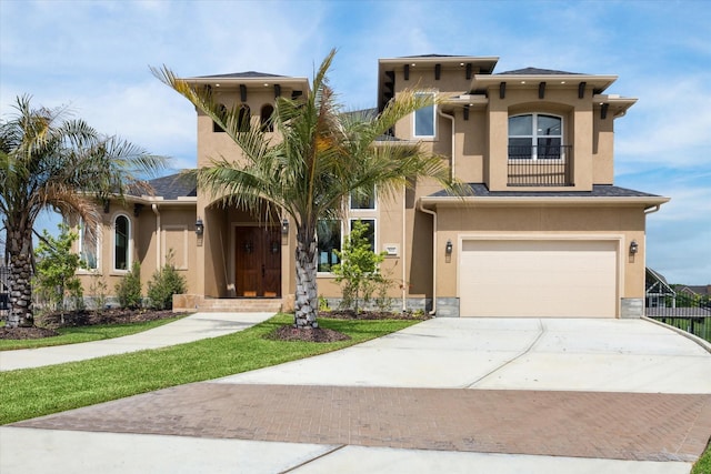 view of front of house featuring decorative driveway, stucco siding, an attached garage, a balcony, and stone siding