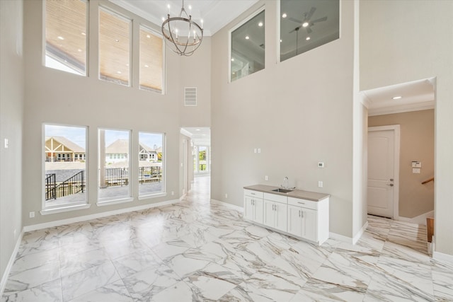 unfurnished living room with ornamental molding, a towering ceiling, light tile patterned floors, sink, and a notable chandelier