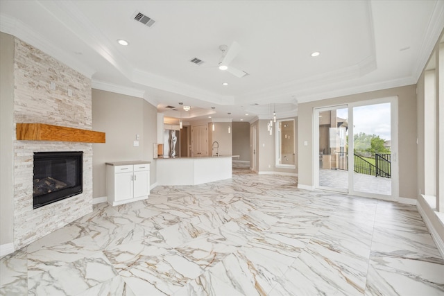 unfurnished living room featuring ceiling fan, a raised ceiling, a stone fireplace, light tile patterned floors, and crown molding