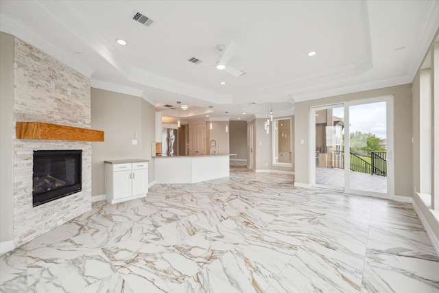 unfurnished living room featuring visible vents, a raised ceiling, crown molding, and a stone fireplace