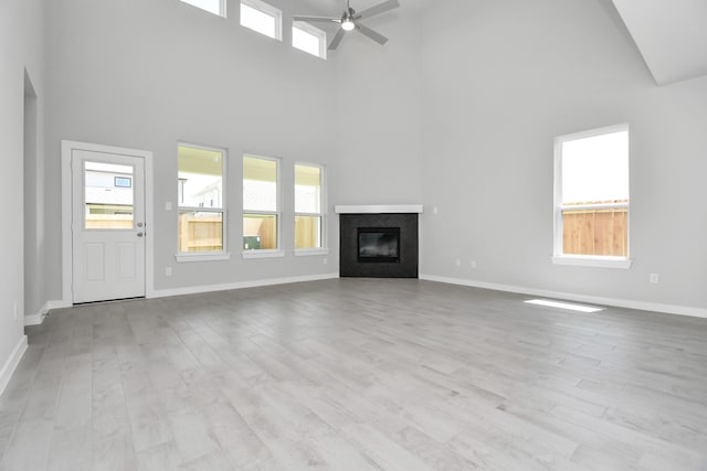 unfurnished living room with ceiling fan, light hardwood / wood-style floors, and a high ceiling