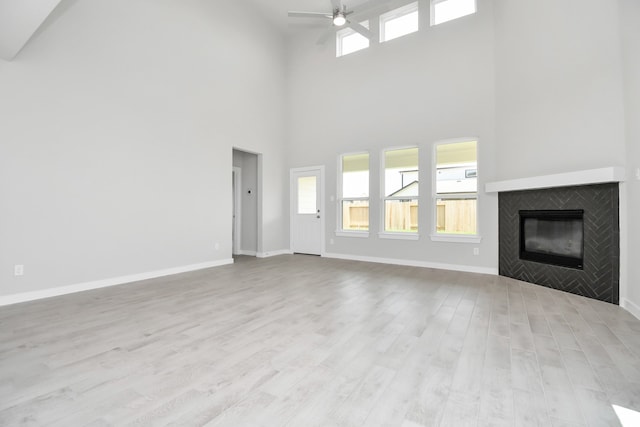 unfurnished living room featuring ceiling fan, a high ceiling, light hardwood / wood-style flooring, and a fireplace