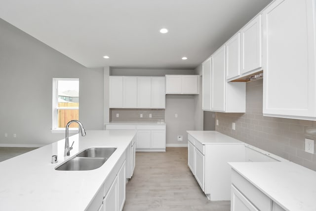 kitchen with backsplash, light hardwood / wood-style floors, white cabinets, and sink