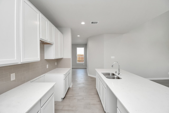 kitchen featuring sink, light hardwood / wood-style flooring, white cabinetry, and backsplash