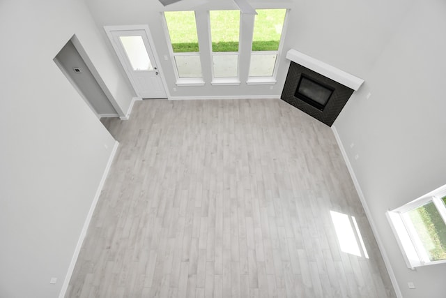 unfurnished living room featuring light wood-type flooring, a high ceiling, and a healthy amount of sunlight