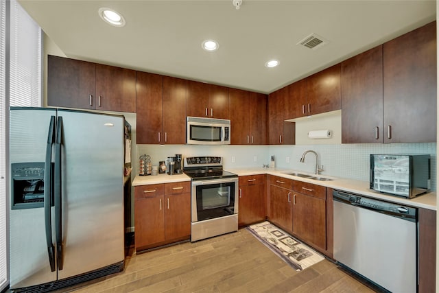 kitchen featuring stainless steel appliances, light hardwood / wood-style floors, tasteful backsplash, and sink