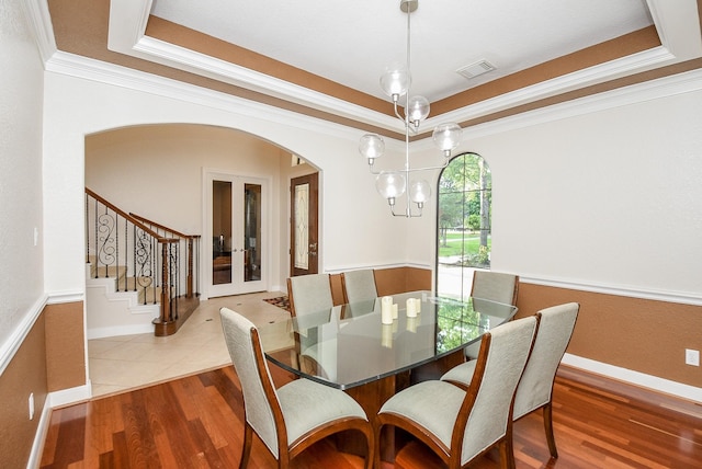 dining room with crown molding, wood-type flooring, a tray ceiling, and an inviting chandelier