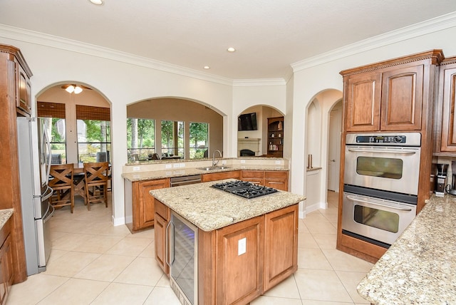 kitchen featuring light tile patterned floors, ornamental molding, a kitchen island, appliances with stainless steel finishes, and light stone countertops